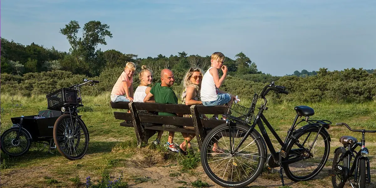 Gezin op een bankje in de duinen met fietsen eromheen