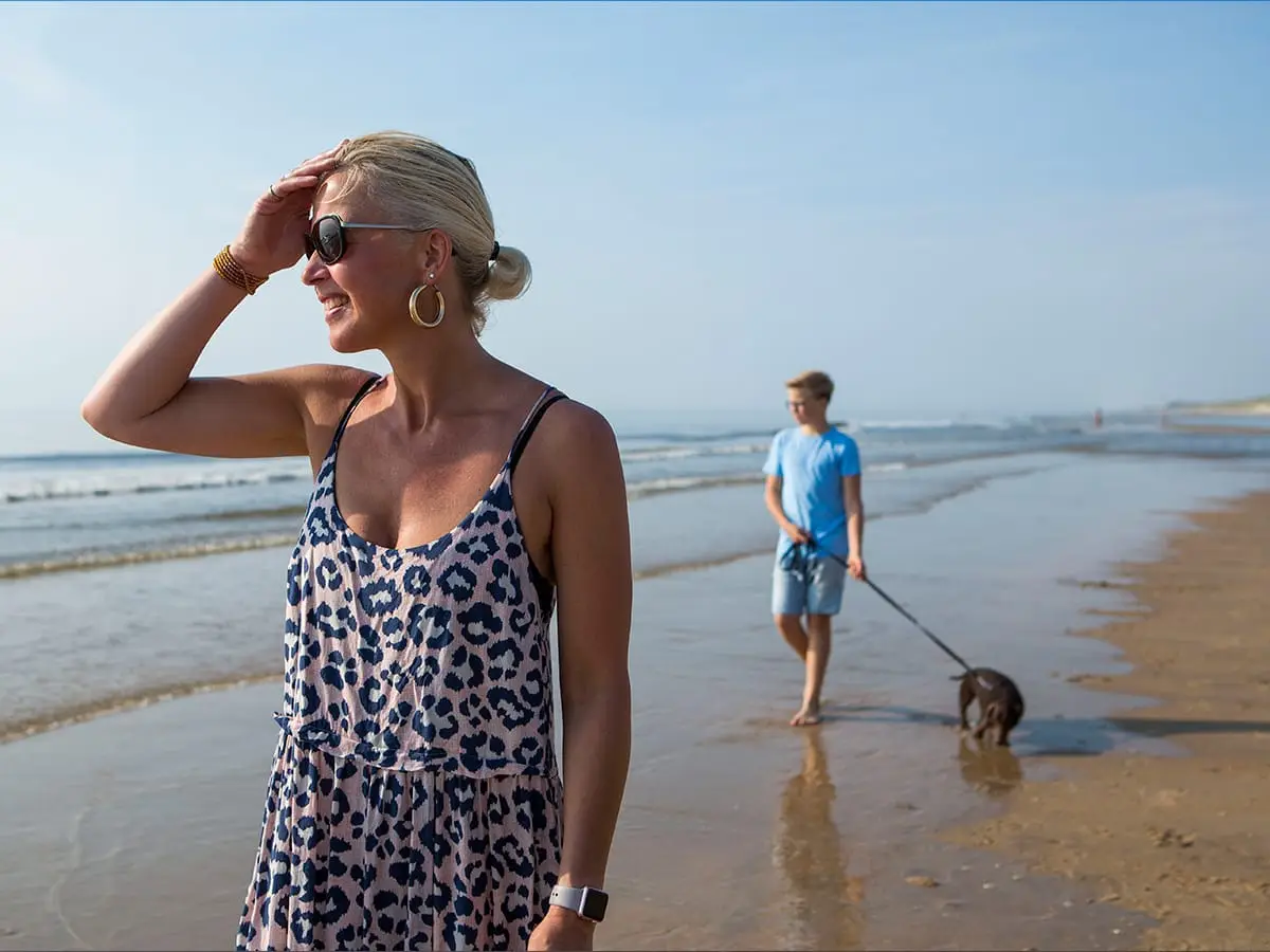 Moeder en zoon lopen met de hond op het strand