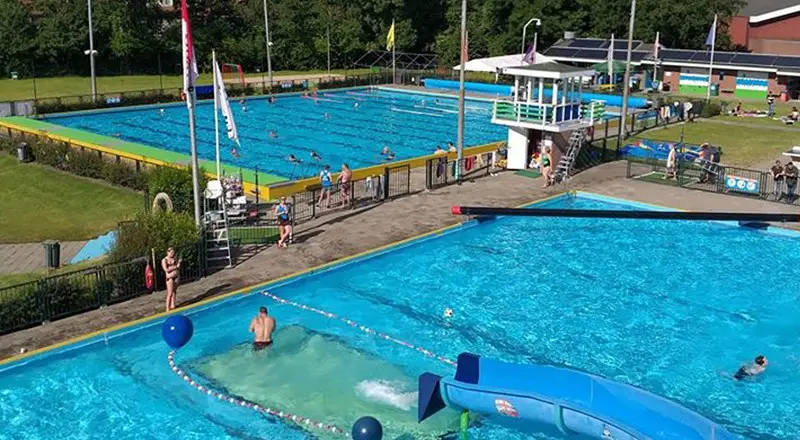 Het openlucht zwembad van boven, je ziet twee baden en een glijbaan