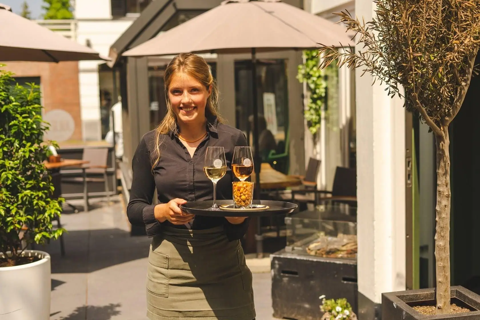 Serveerster met een dienblad met twee glazen wijn en borrelnoten