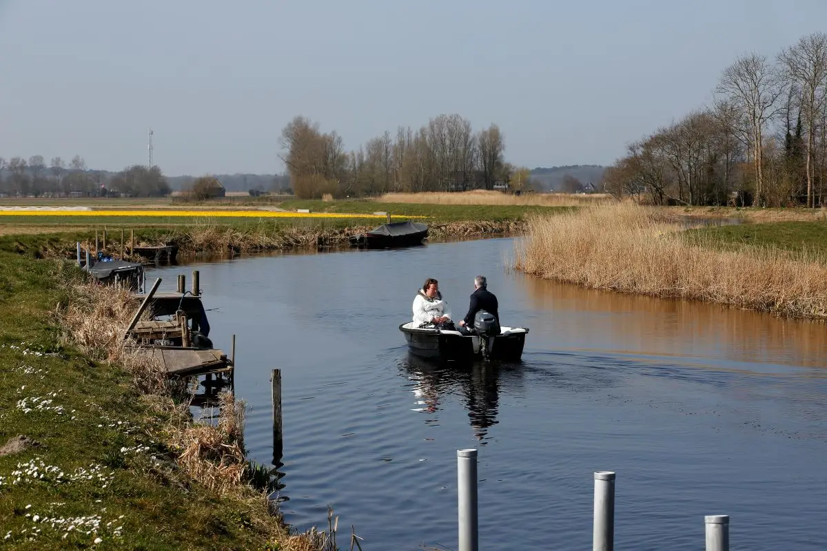 Een stel varend op een bootje door de polders in Bergen met riet langs de kant en bomen in de verte