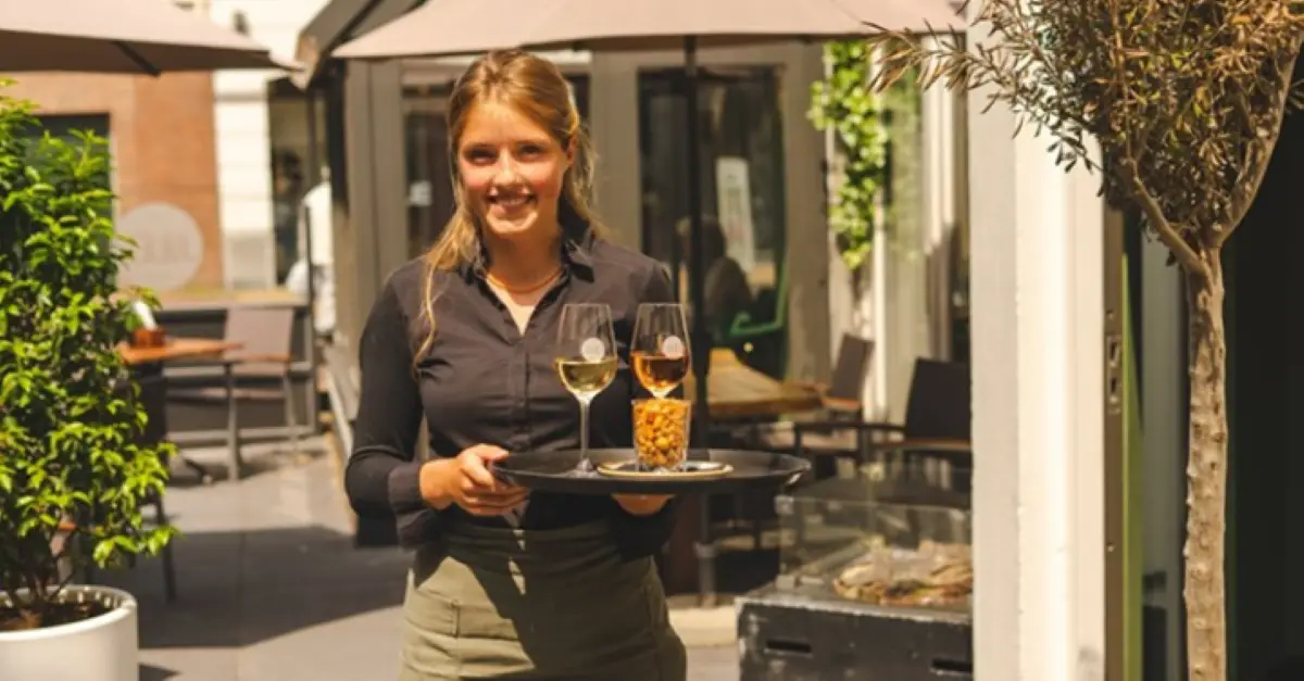 Een bedienster met een dienblad met twee glazen wijn en nootjes