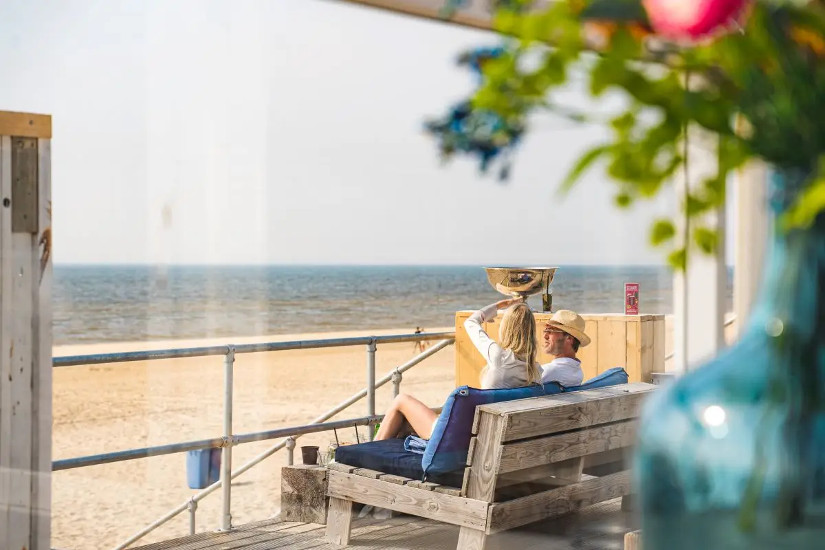 twee mensen op een houten bank kijkend naar het strand