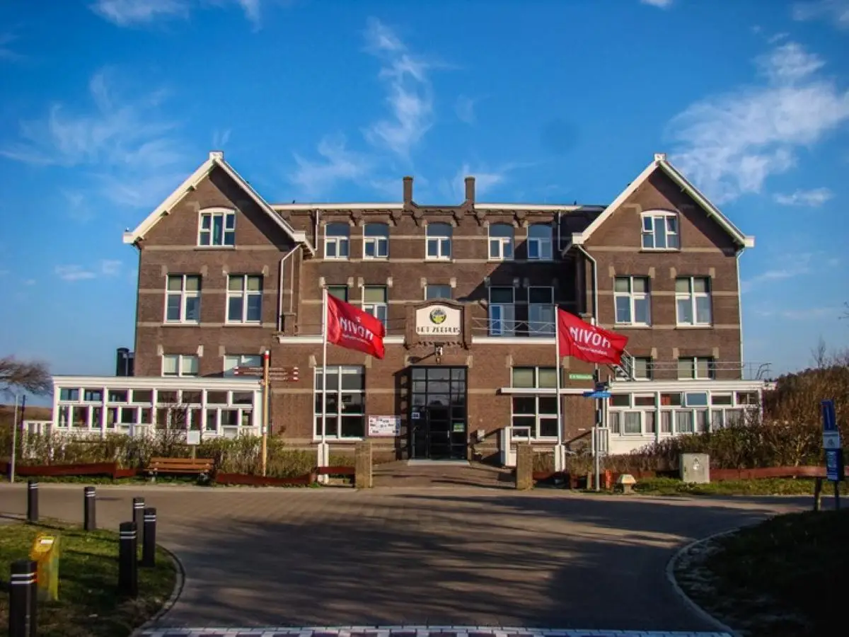 Vooraanzicht van Het Zeehuis, een groots huis van steen met vele witte kozijnen en ramen aan zee met blauwe lucht