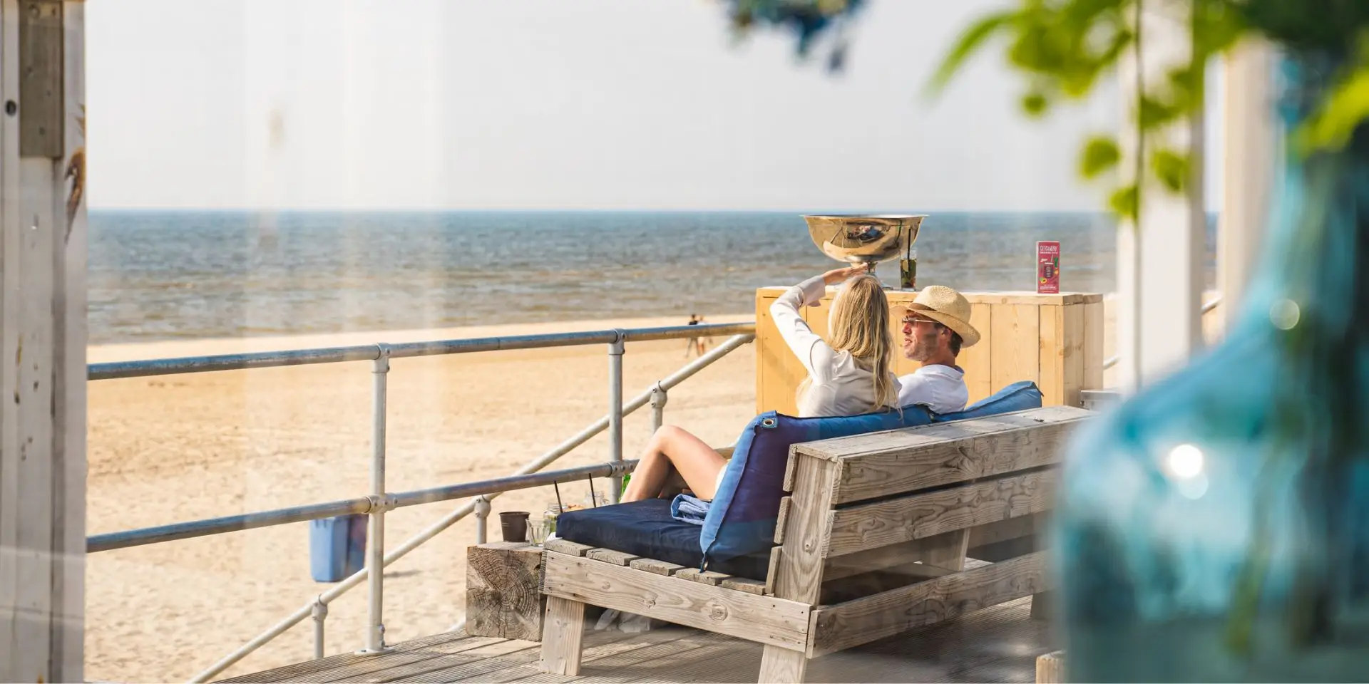 twee mensen op een houten bankje kijkend naar het strand en de zee