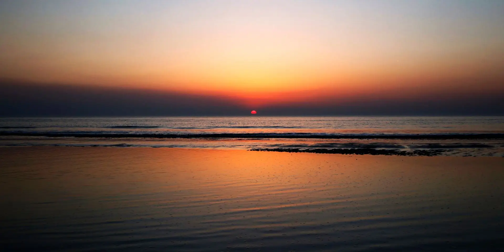 Zonsondergang met rode, oranje en gele tinten op het strand en zee in Bergen aan Zee
