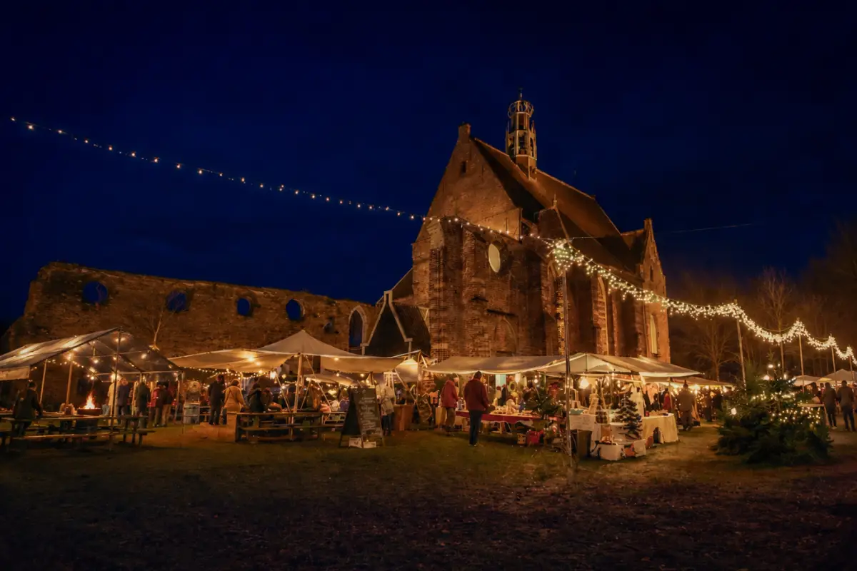 Avondmarkt bij de Ruïnekerk met verlichte kraampjes, sfeervolle lichtslingers en bezoekers rondom de historische kerk.