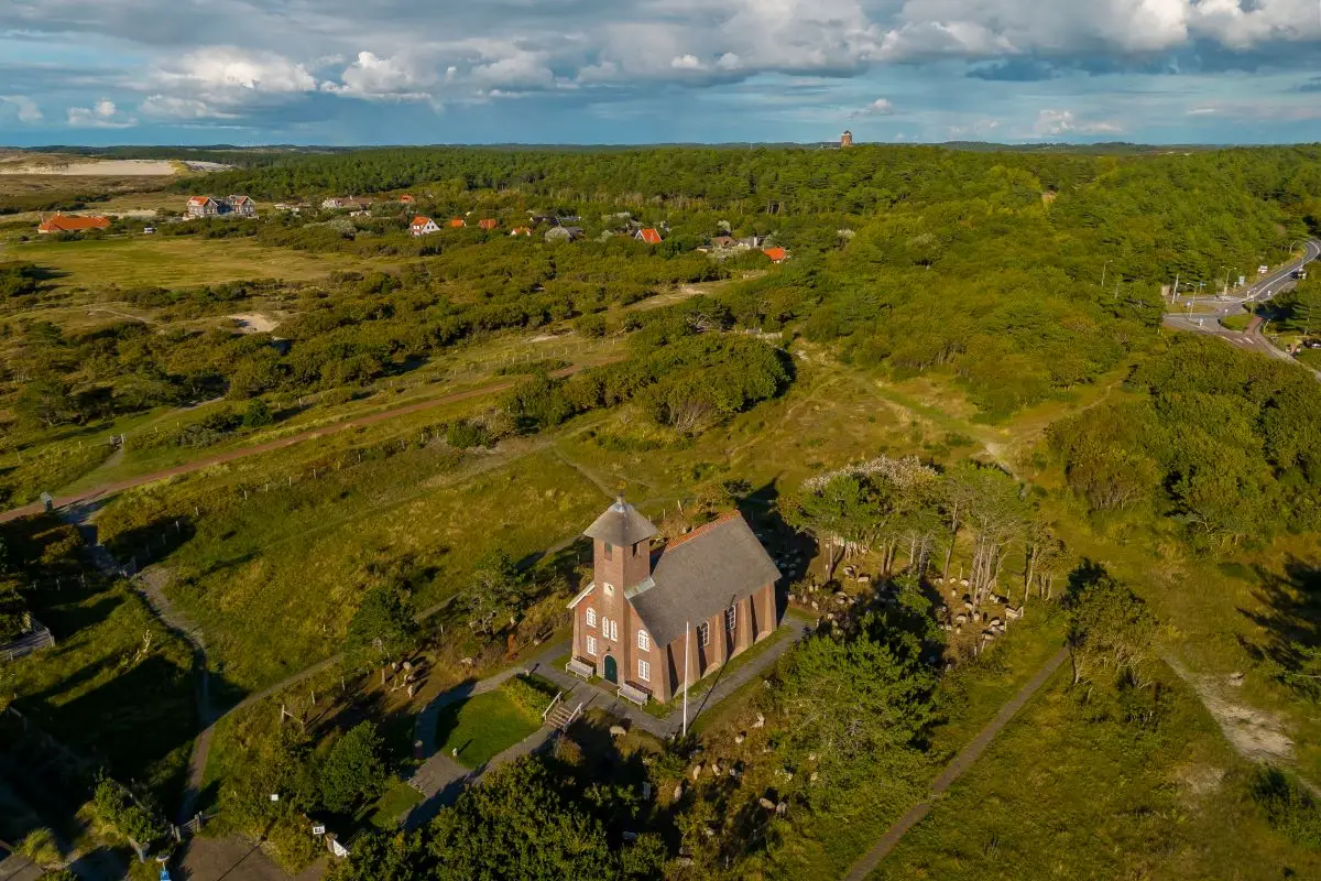 Luchtfoto van het Vredeskerkje in Bergen aan Zee met omliggende bomen en het dorp