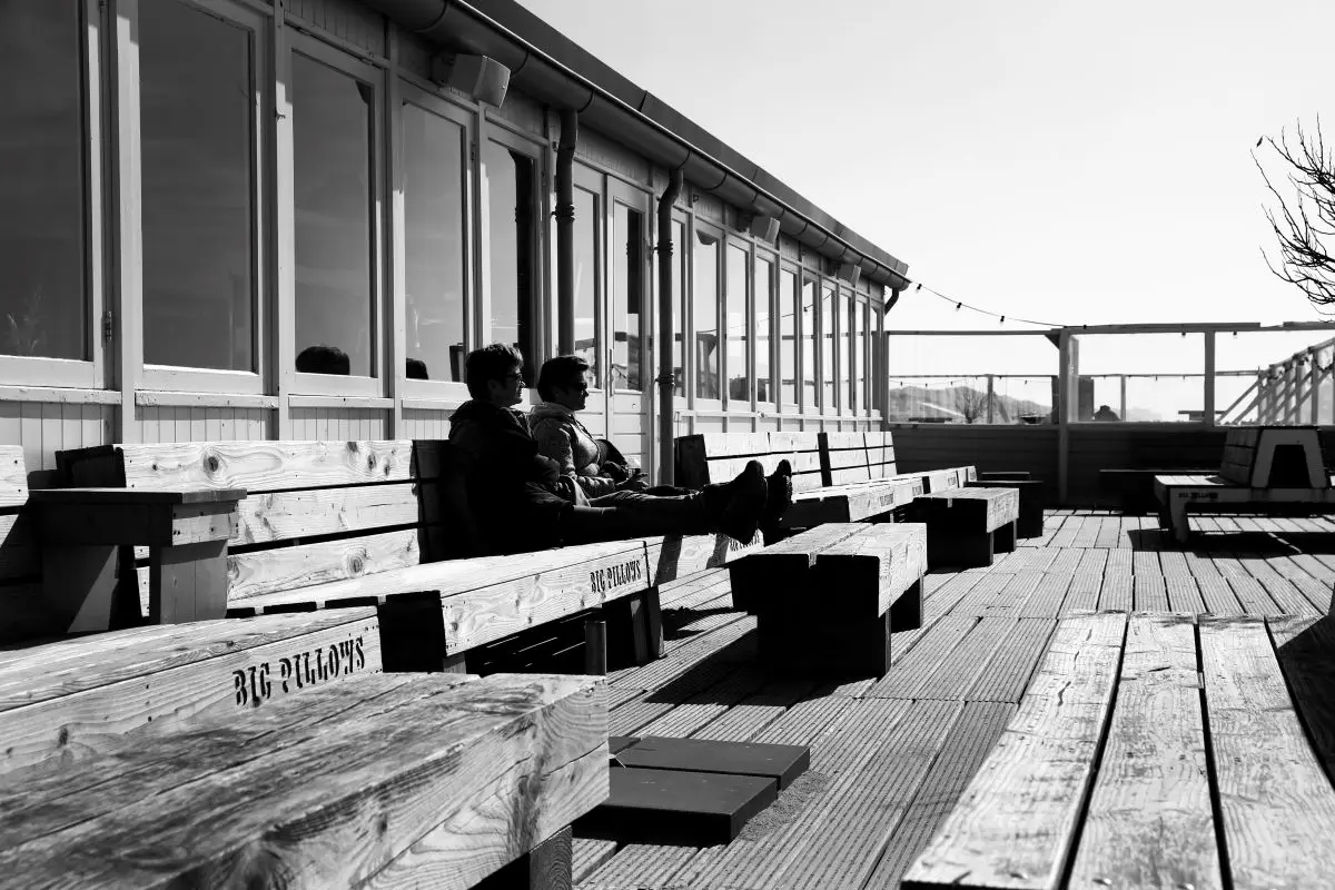 Twee mensen zittend aan het genieten bij een strandpaviljoen op een houten bank op het terras