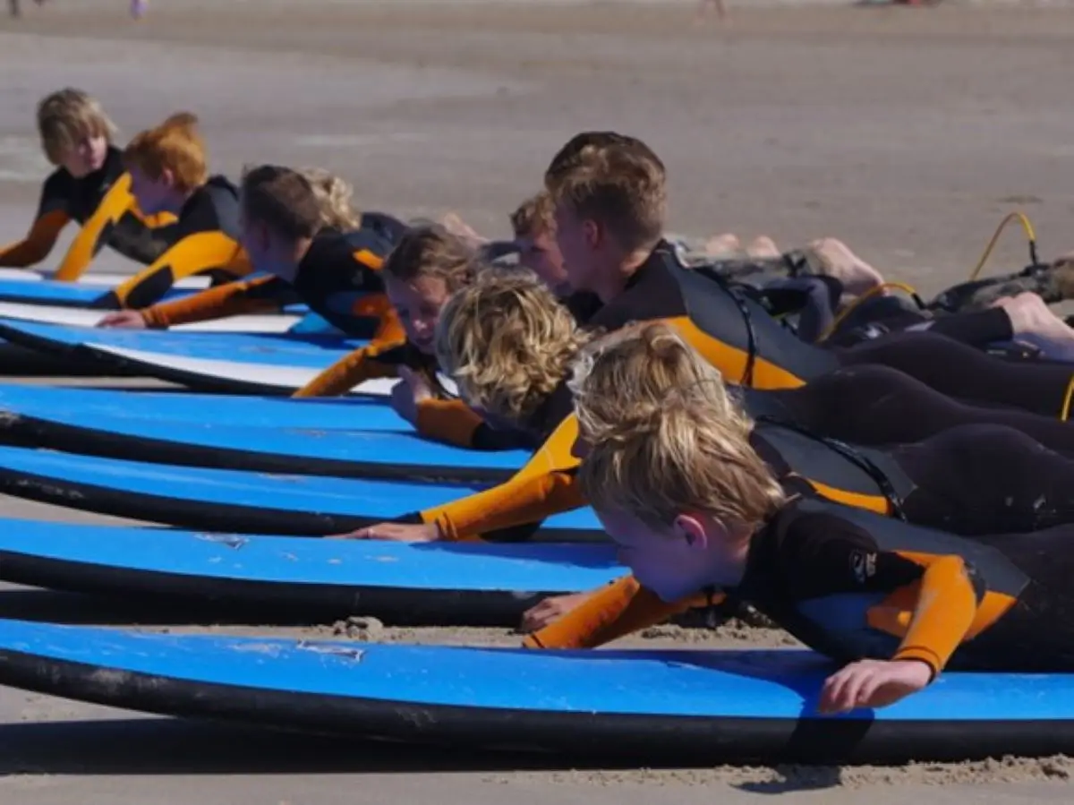 9 kinderen in een zwemsuit op blauwe surfplanken tijdens surflessen in Bergen aan Zee