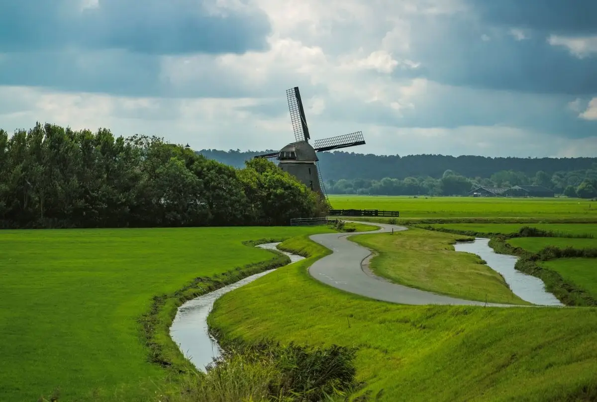 Molen in de polder met een kronkelende dijk en groene weilanden met donkere wolken