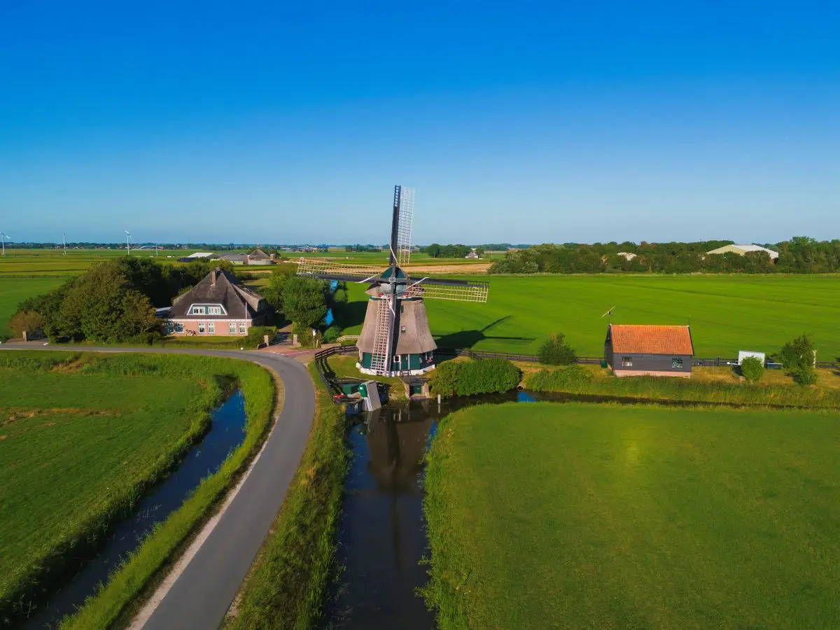 Luchtfoto van de Groetermolen met omliggende boerderij en molenhuisje in de polder met een dijkje op een zomerse dag met blauwe lucht