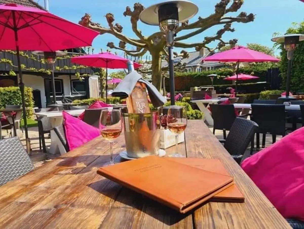 Tafel met wijnglazen en menukaarten op het buitenterras bij de Bokkesprong met roze parasols op een zonnige dag