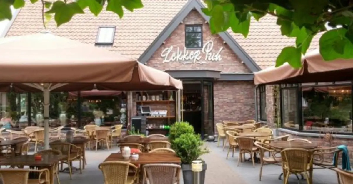 Het terras bij Restaurant Lekker Puh met vooraanzicht van het restaurant met meerdere tafels en rieten stoelen en grote parasols