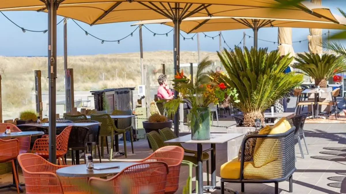 Het buiten terras bij strandpaviljoen Struin met gekleurde stoelen, kussens, parasols, gezellige lichtjes en tafels. Met uitzicht op het duingebied.