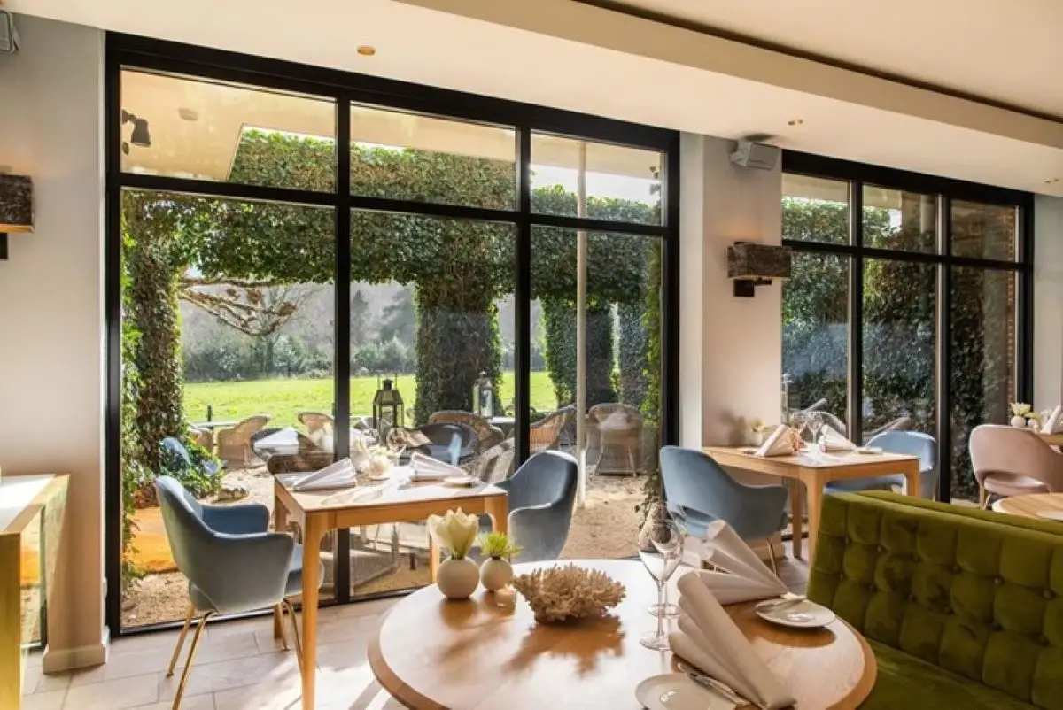 Binnenkant van Restaurant Hotel Merlet met chique gedekte tafels en uitzicht op de tuin
