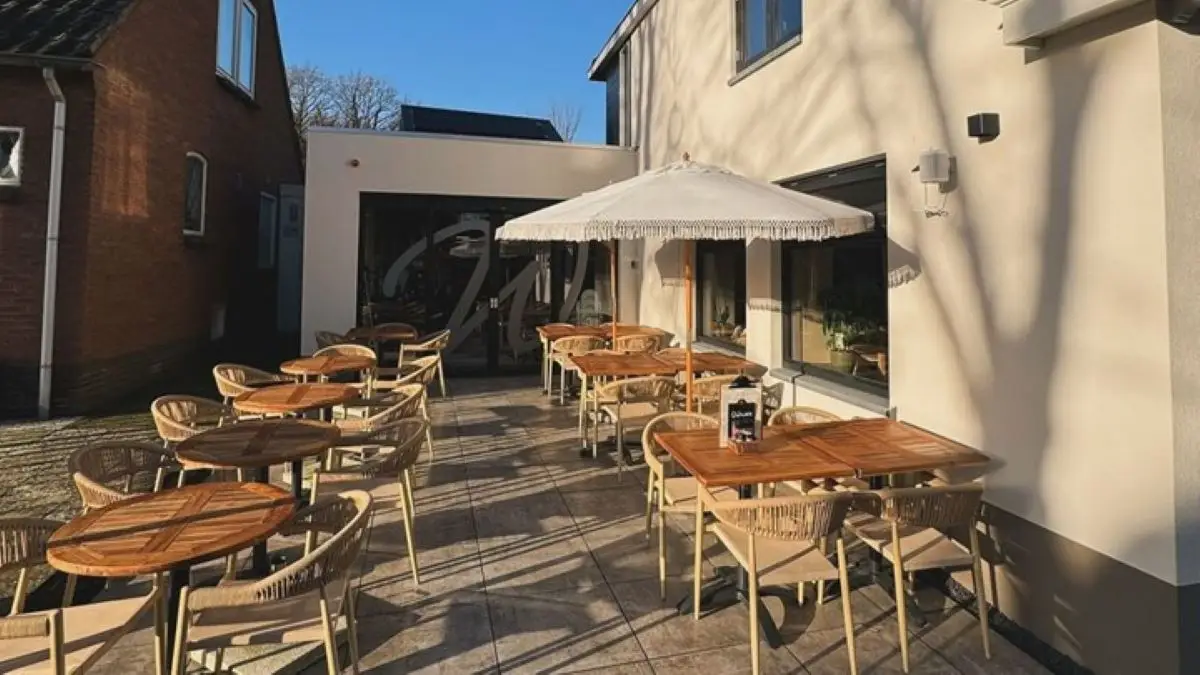 Terras bij WideWood met meerdere tafels en stoelen en een witte parasol.