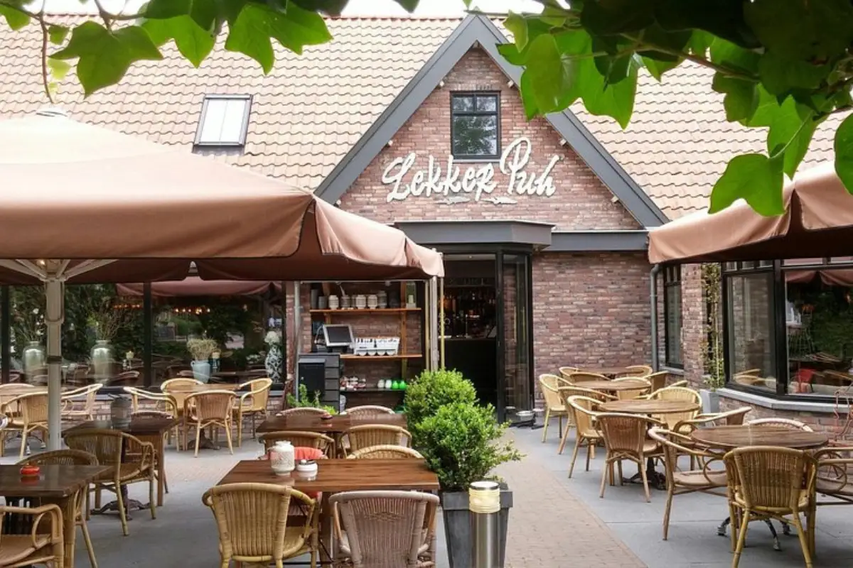 Het terras bij Restaurant Lekker Puh met vooraanzicht van het restaurant met meerdere tafels en rieten stoelen en grote parasols