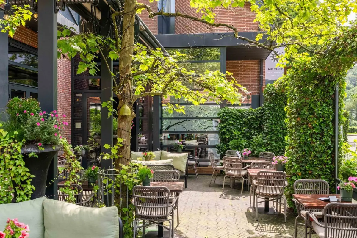 Terras van Restaurant Hotel Merlet met chique gedekte tafels en uitzicht op de tuin
