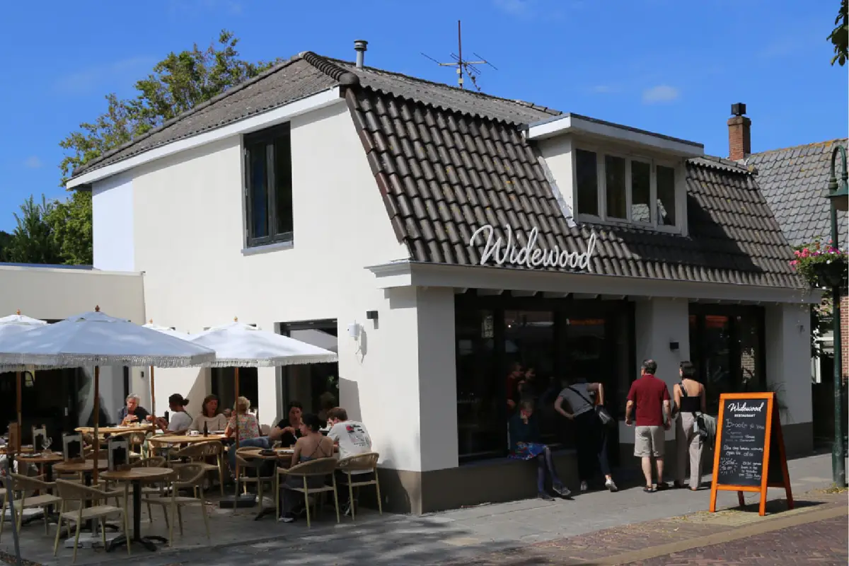 Terras bij WideWood met meerdere tafels en stoelen en een witte parasol.