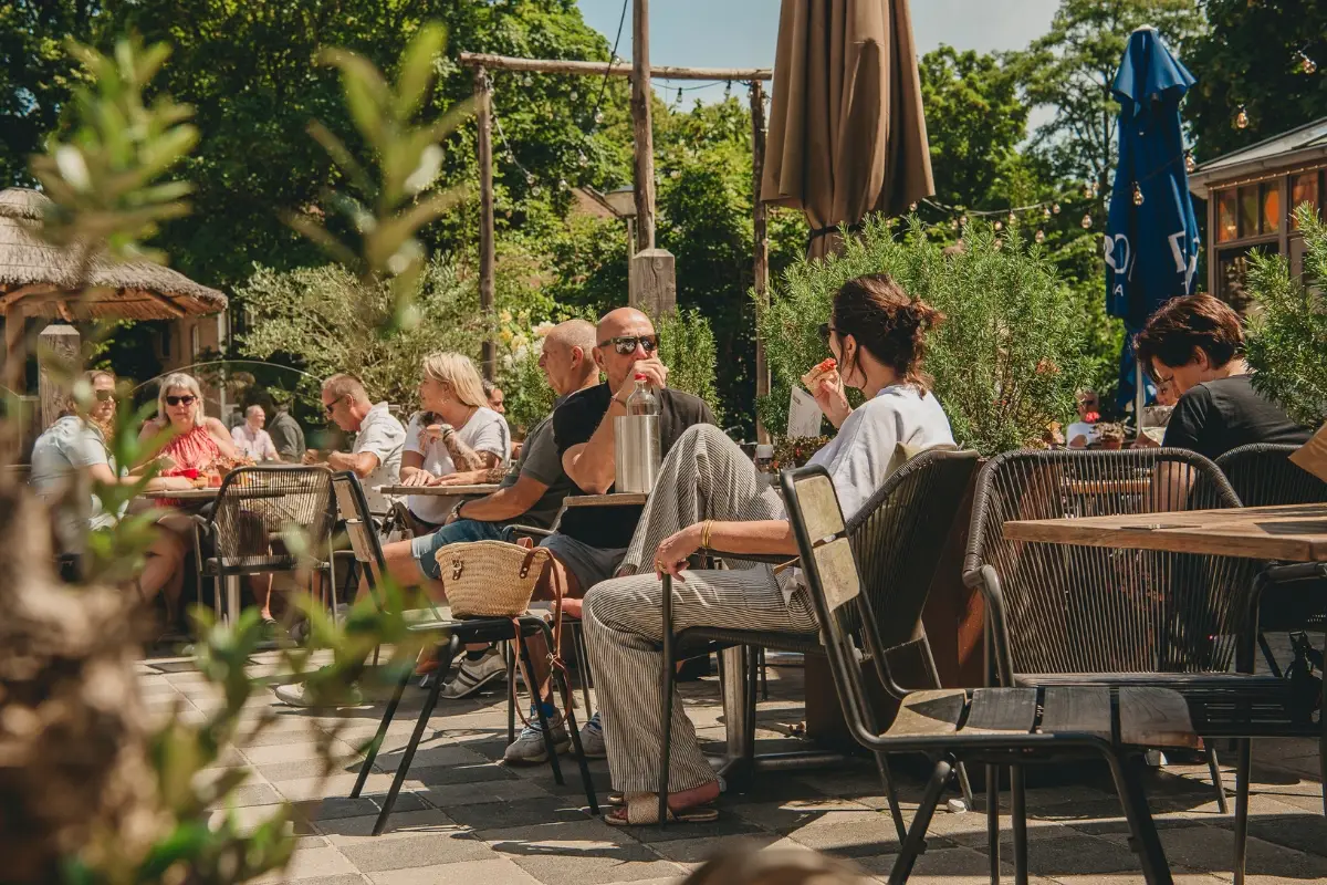 Bezoekers genieten op een zonnig terras in Schoorl met uitzicht op het Klimduin, omringd door groen en zomerse gezelligheid.