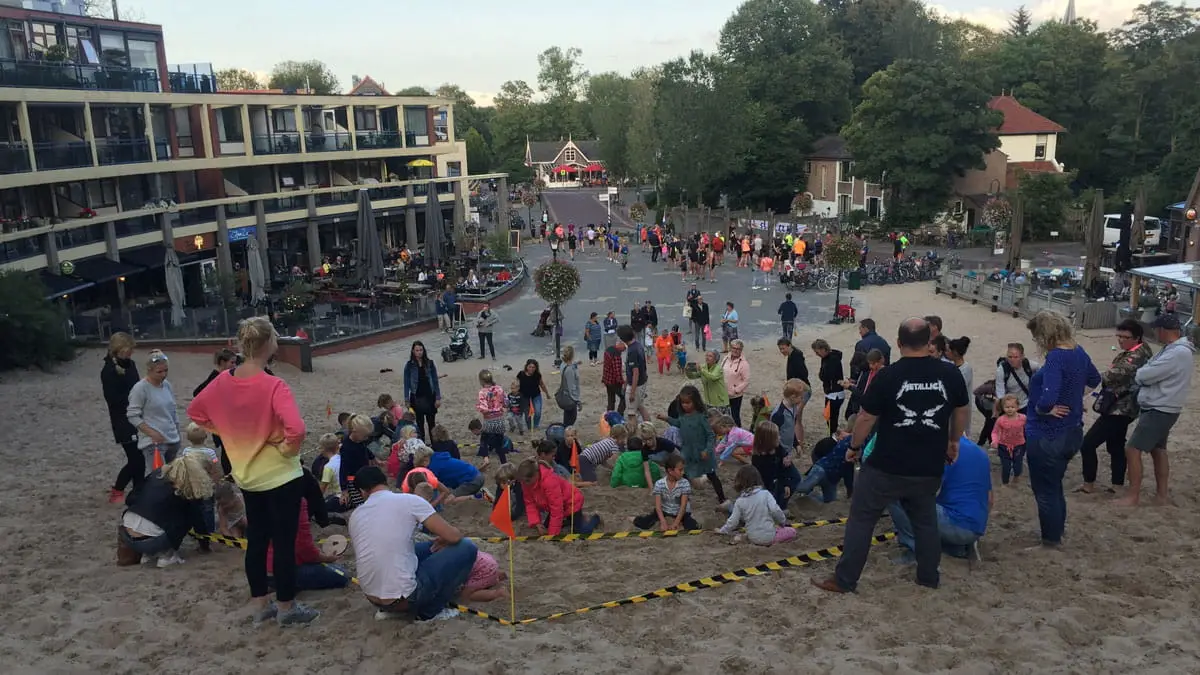 Foto van de activiteit schatgaven op het Klimduin met veel kinderen en het centrum van Schoorl op de achtergrond