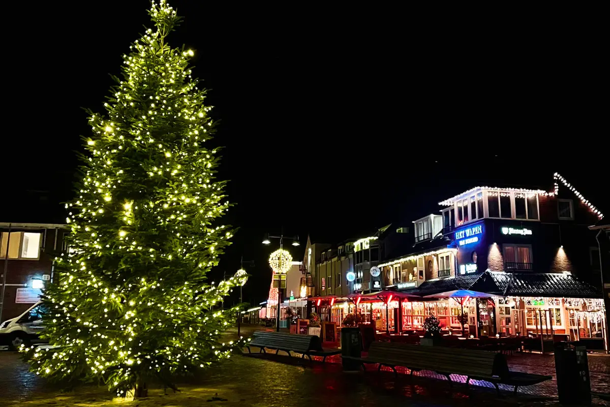 Sfeervol plein in Egmond aan Zee tijdens de wintermaanden met een grote verlichte kerstboom, feestelijk verlichte horeca en warme verlichting in de straat. De gezellige avondsfeer benadrukt het bruisende en gastvrije karakter van de historische familiebadplaats.
