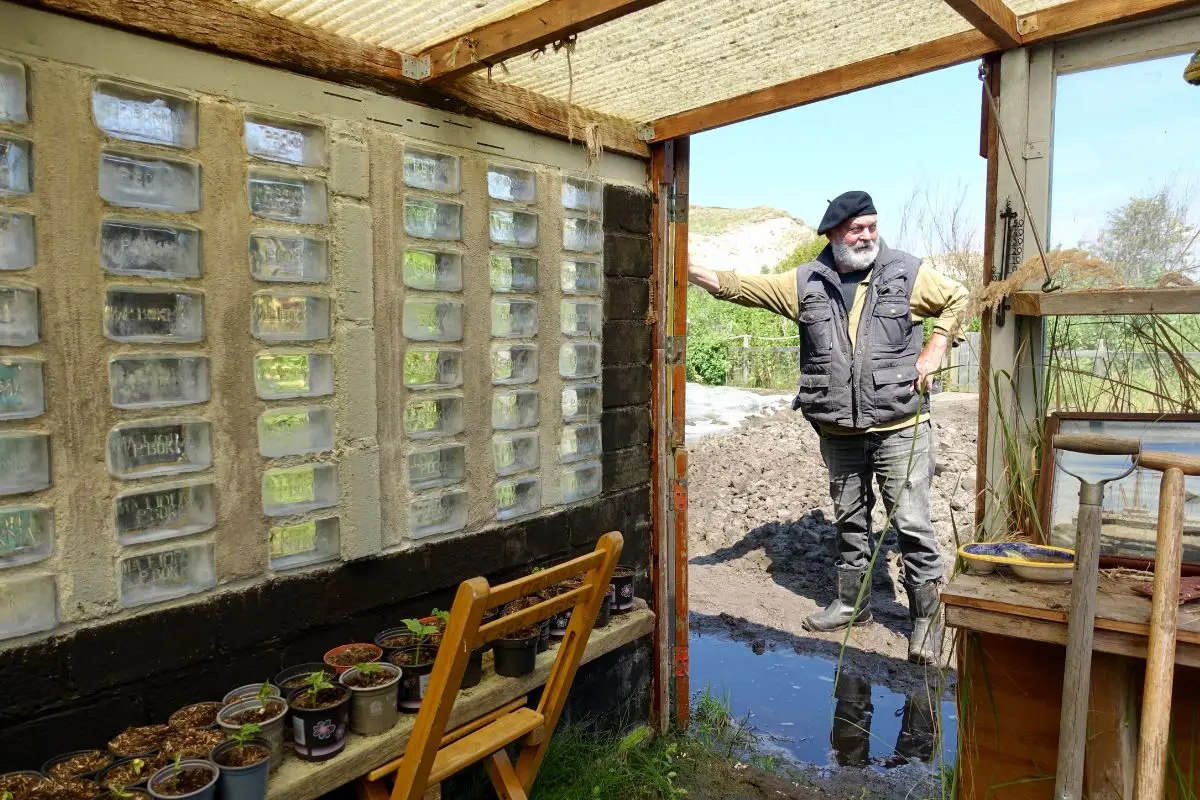 Kleine kas met planten in potjes met  een man in de deuropening
