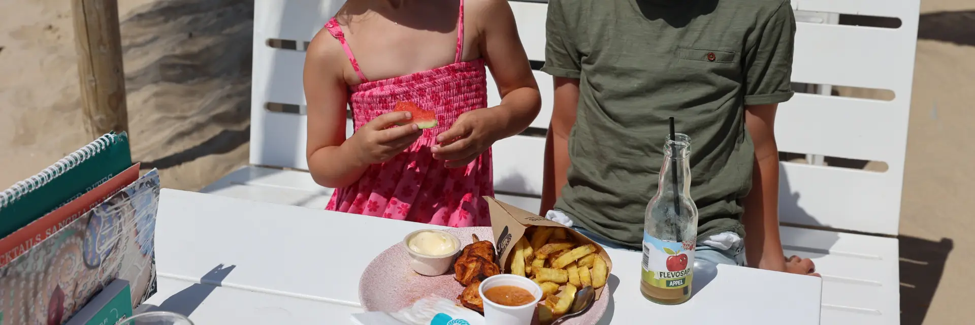 Houten hek van paaltjes op het strand van Egmond aan Zee met op de achtergrond het duin op een mooie zomerse dag met blauwe lucht