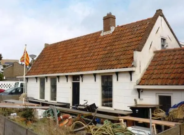 Een wit, oude vissershuisje met rode daken en Egmondse vlag