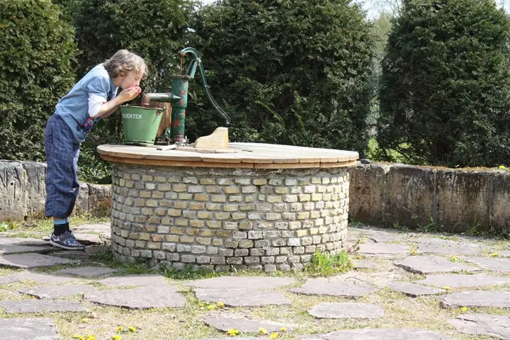 Jongen drinkt met zijn handen water uit de stenen, ronde put van de Adelbertusakker