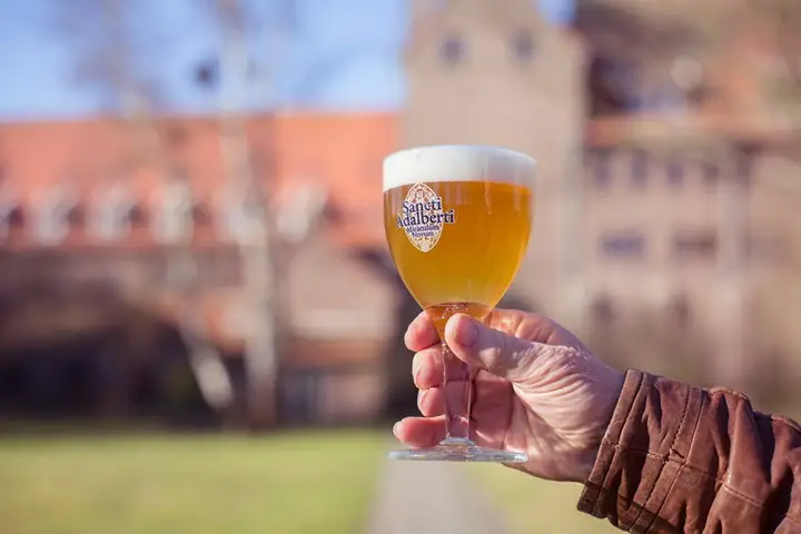 Goudgeel biertje van Brouwerij Egmond in de hand met op de achtergrond de Abdij van Egmond