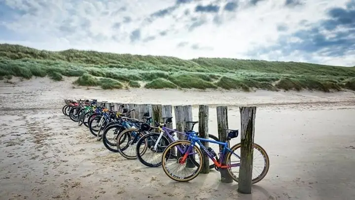 Fietsen op het strand tussen houten palen in Egmond aan Zee met het duin op de achtergrond en blauwe lucht