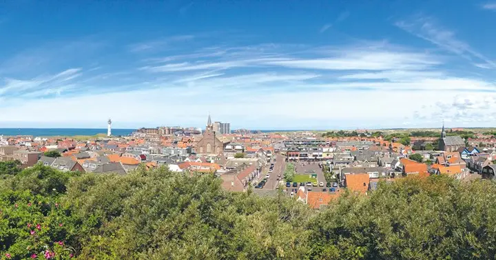 Uitzicht over Egmond aan Zee op een zonnige dag met de huizen en in de verte de witte vuurtoren J.C.J. van Speijk en de kerken