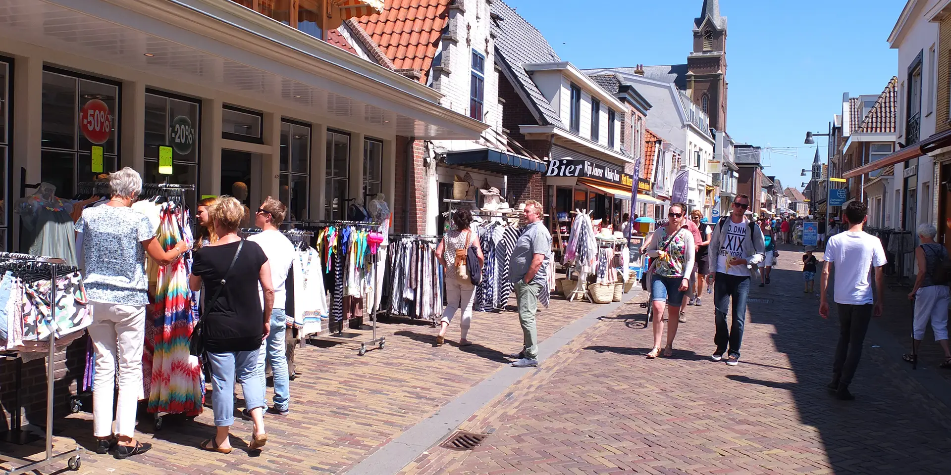 Foto van de Voorstraat in Egmond aan Zee met winkelende mensen en winkels met kledingrekken