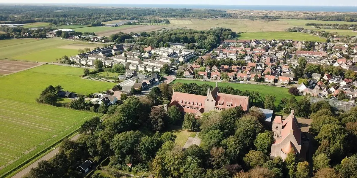 Luchtfoto van de Abdij van Egmond en het dorp Egmond-Binnen met in de verte de duinen, bossen en de zee