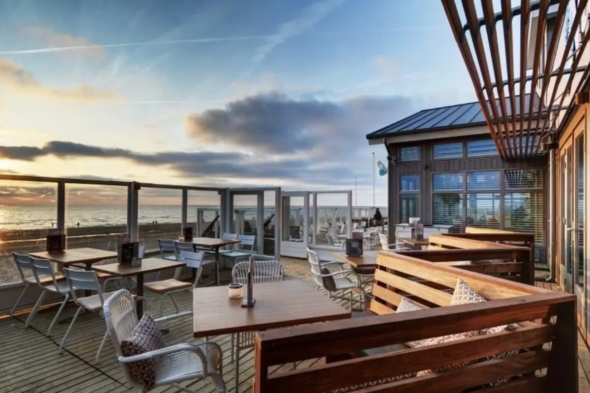 Terras met tafels en stoelen van strandpaviljoen Nautilus aan Zee met zicht op het strand en de zee