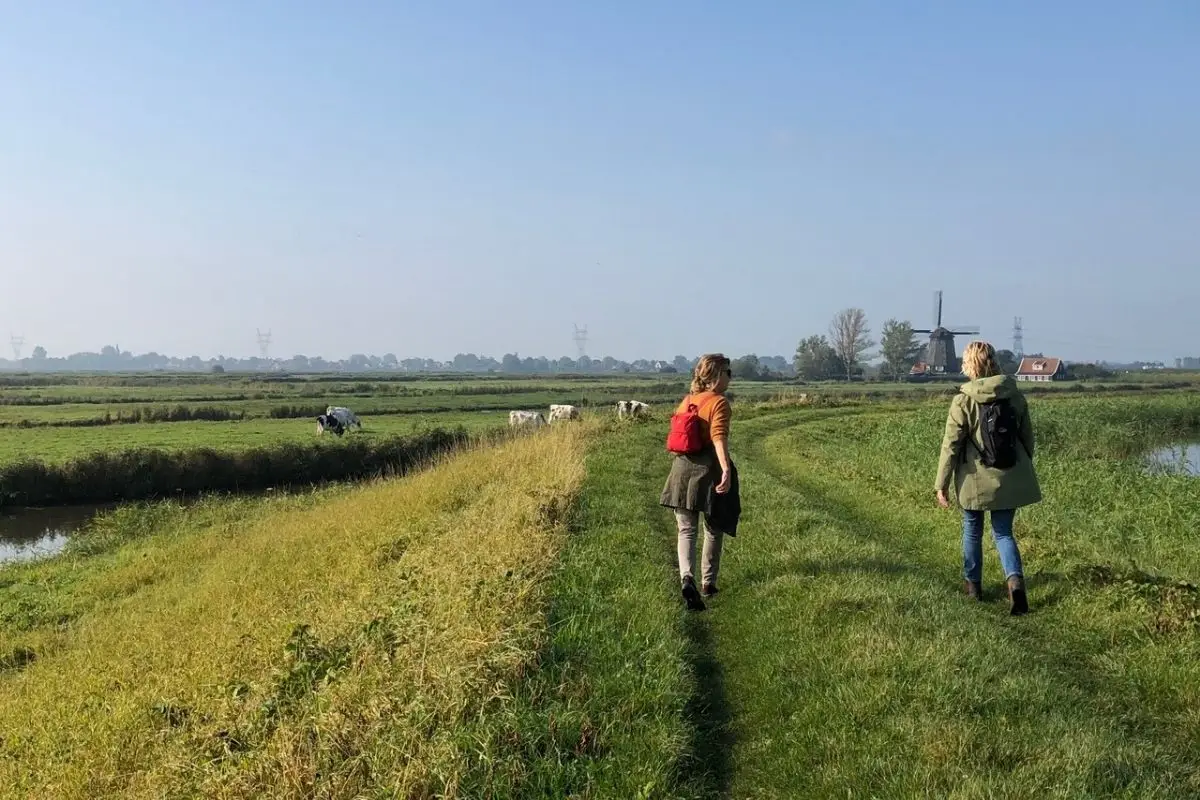 Twee vrouwen wandelend over weilanden met een molen op de achtergrond