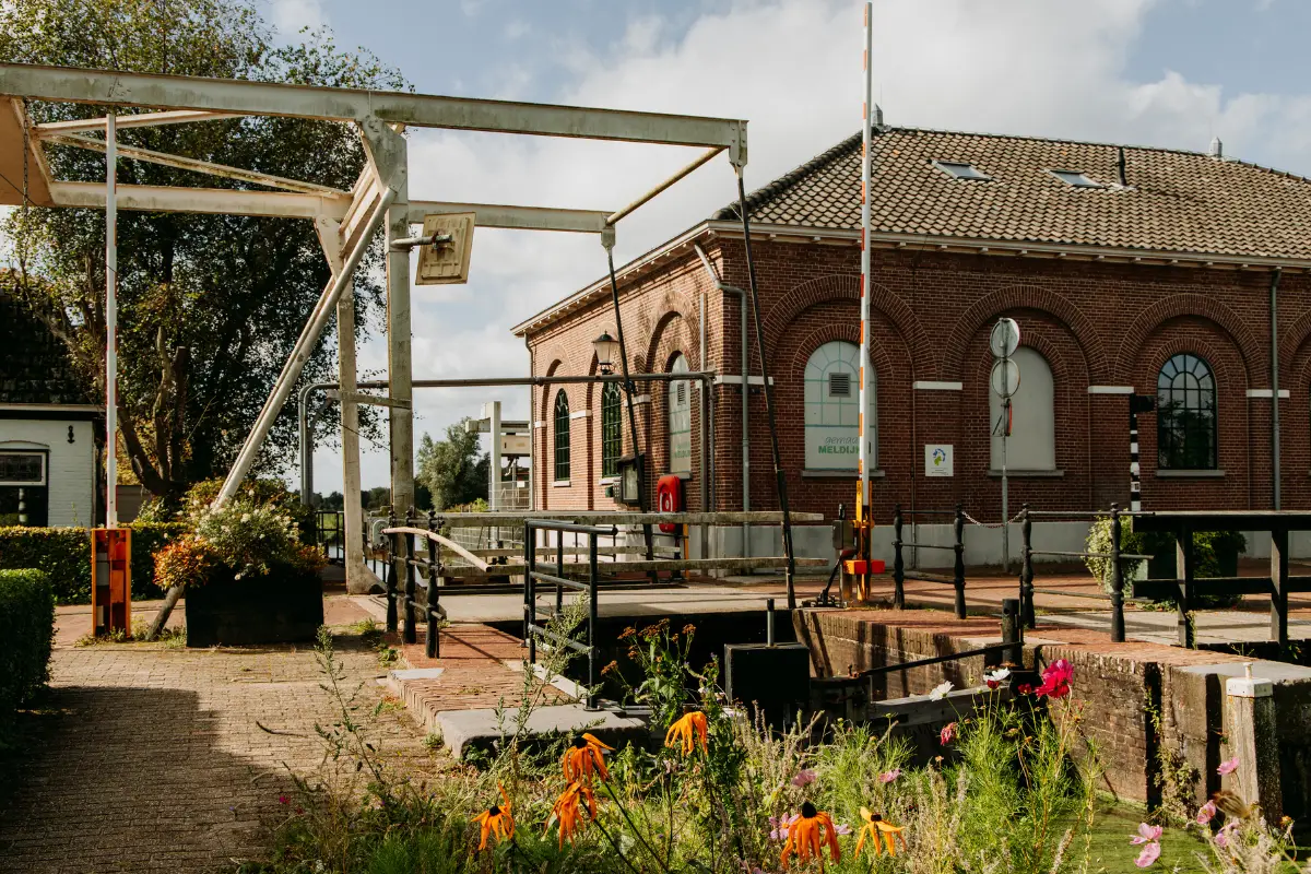 Gemaal Meldijk. een monumentaal stenen pand met witte ophaalbrug en verschillende bloeiende planten en bloemen